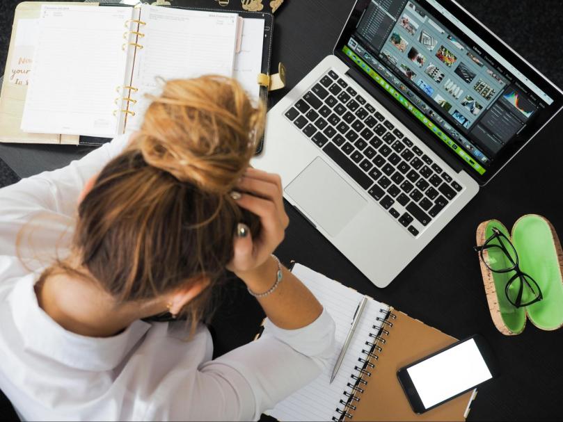Top-down view of person with head in hands at their desk.